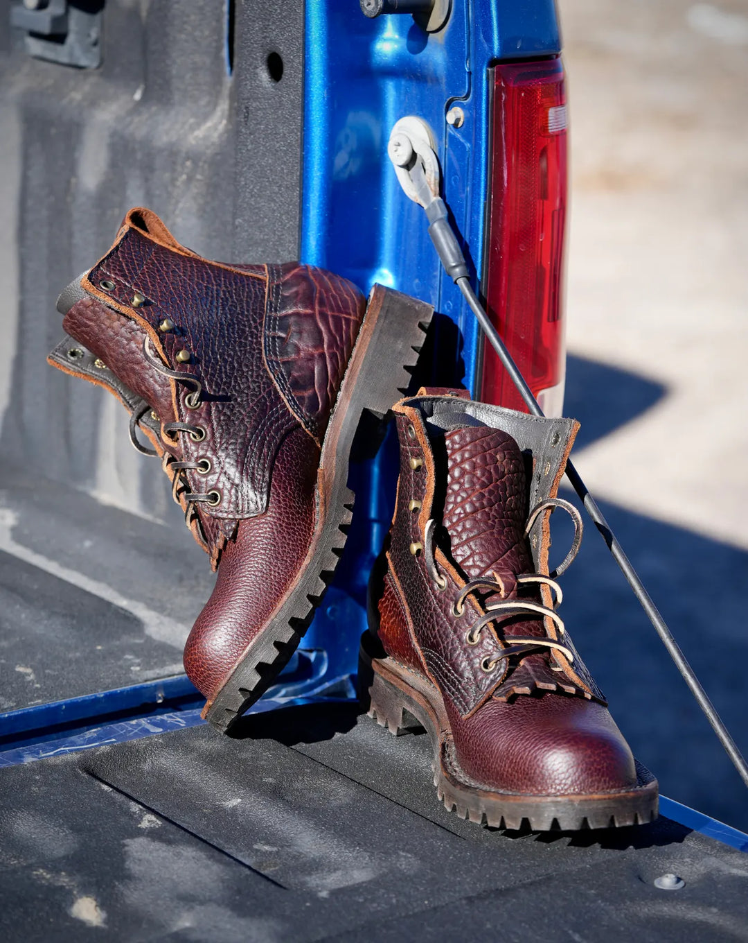 A pair of brown bison leather work boots with laces sitting on the tailgate of a blue pickup truck